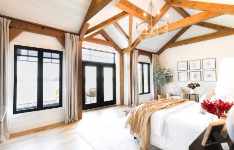 Bedroom with large windows trimmed in black and wood beam accents on white.
