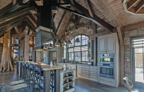 Kitchen with grey cabinets and flooring and stone accent walls and beams.