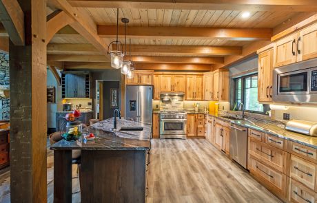 Kitchen view of wood cabinets with black handles and wood flooring. Black/grey/white marbled countertops