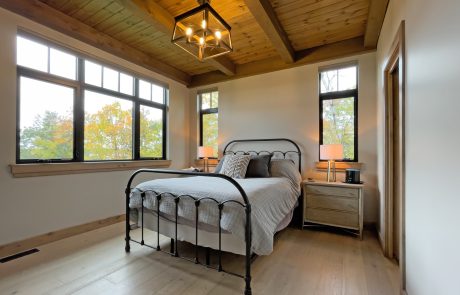 Bedroom with wood ceiling and light wood floors. Windows with black trim